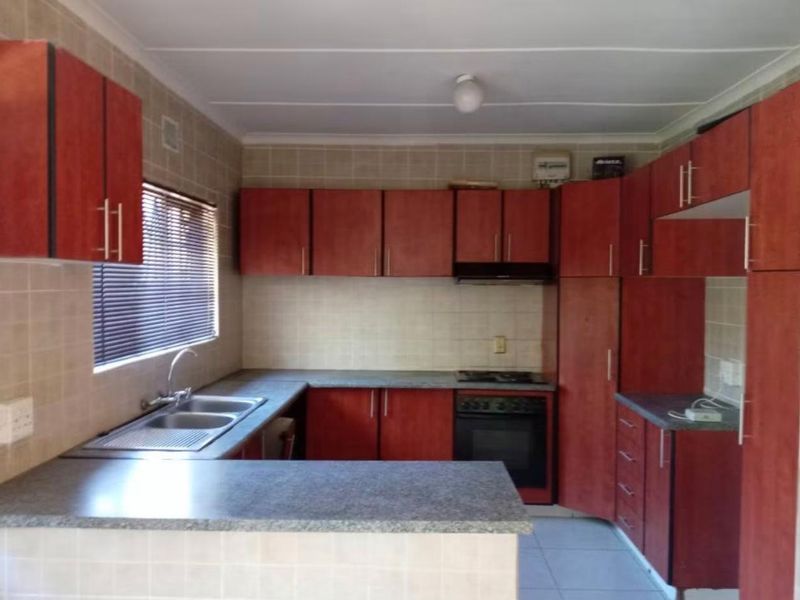 A functional kitchen featuring wood-finish cabinetry, laminate countertops, a double bowl sink, and built-in oven with hob and extractor fan.