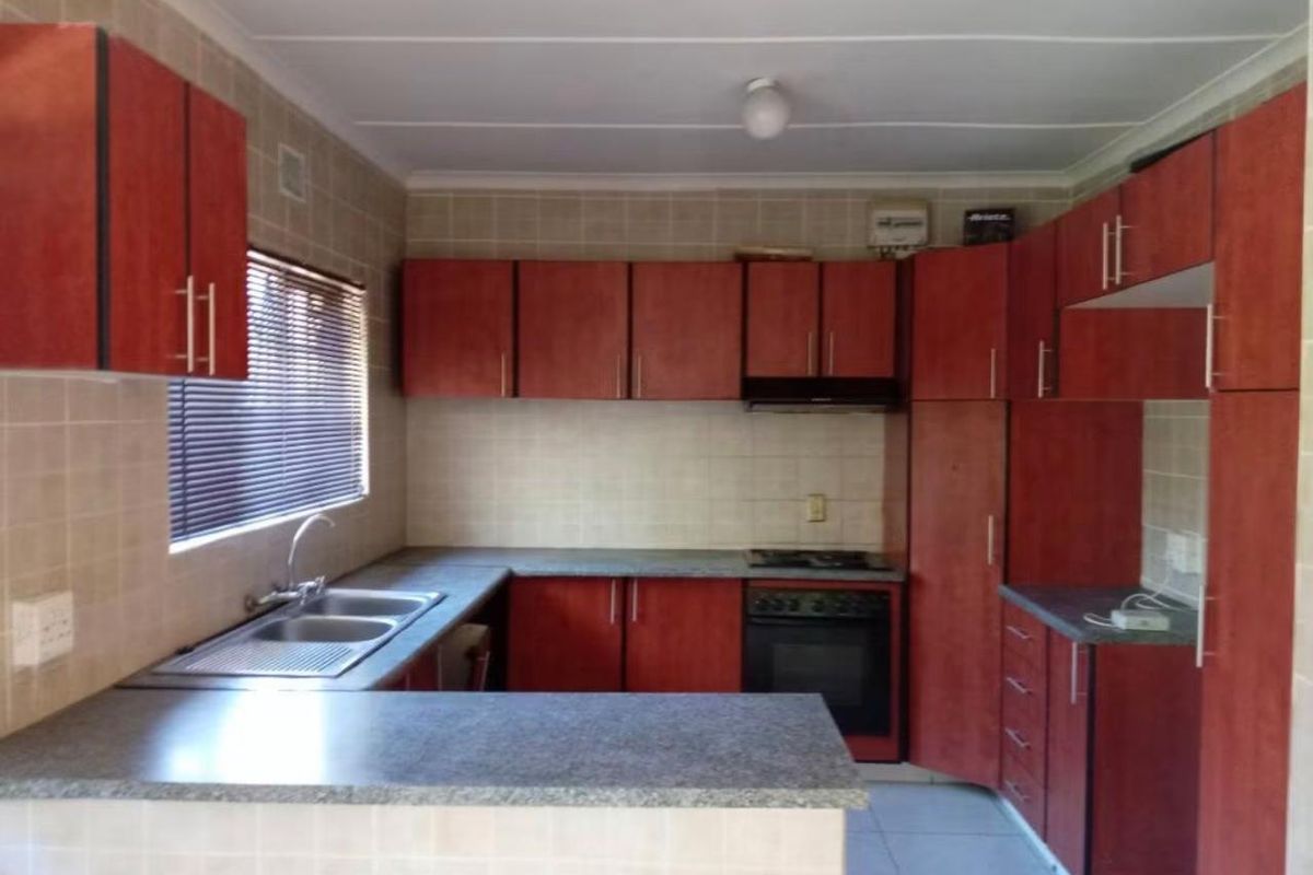 A functional kitchen featuring wood-finish cabinetry, laminate countertops, a double bowl sink, and built-in oven with hob and extractor fan.