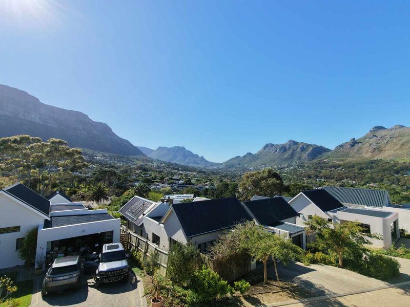 An elevated aerial view of a residential estate featuring modern homes with pitched roofs, paved driveways, and scenic mountain views in the background.