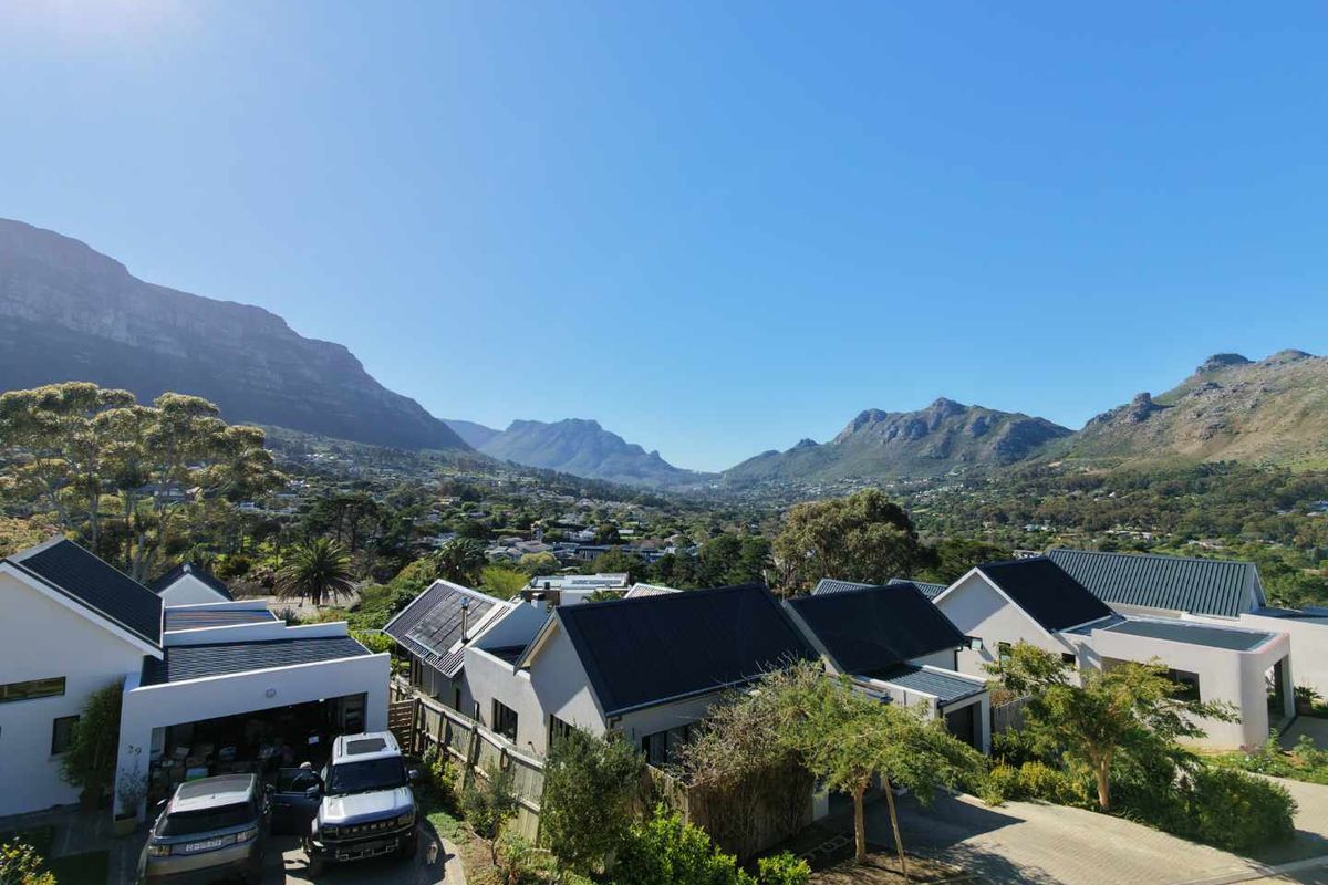 An elevated aerial view of a residential estate featuring modern homes with pitched roofs, paved driveways, and scenic mountain views in the background.