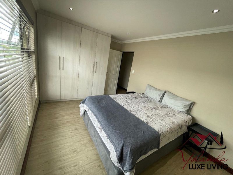 A well-maintained bedroom featuring light-toned laminate flooring, built-in cupboards, recessed downlighting, and venetian blinds.