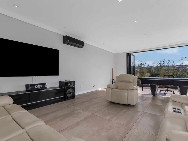 Spacious living room featuring large format floor tiles, recessed downlights, and bi-fold doors opening to an outdoor area.