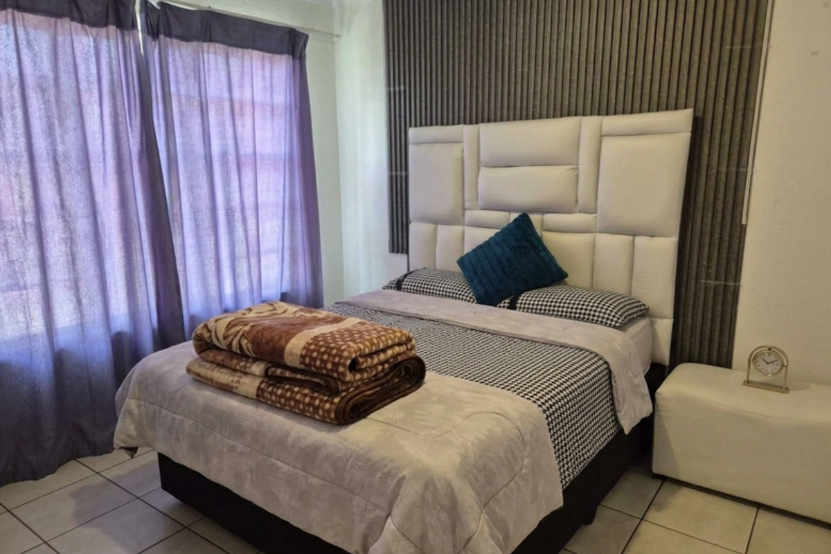 A bedroom featuring tiled flooring and a decorative slatted wall panel behind the bed area.