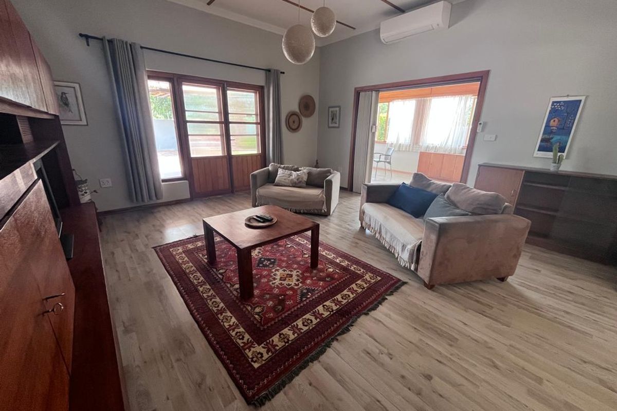 Spacious living room featuring light-toned laminate flooring, timber-framed glass doors leading to an outdoor area, and a wall-mounted split-system air conditioner.