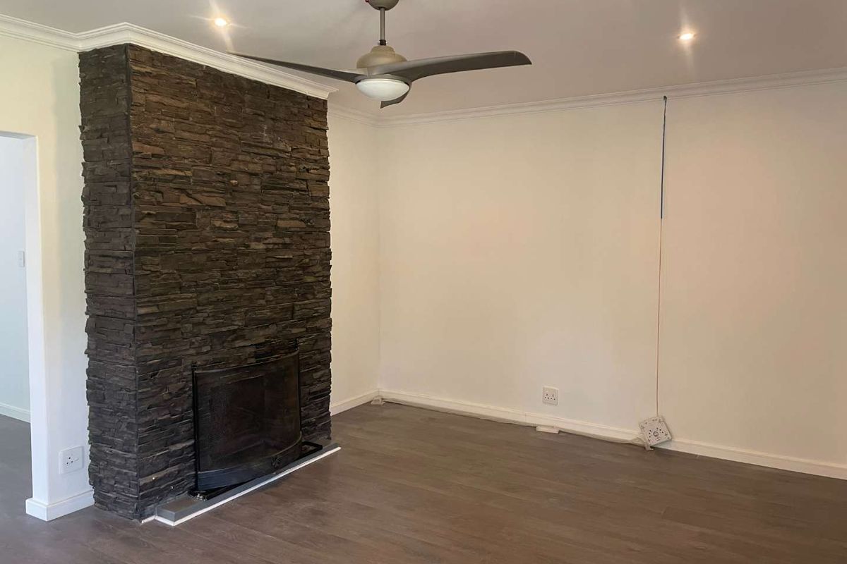A spacious living room featuring a prominent stone-clad fireplace, laminate flooring, and a ceiling fan, offering a neutral canvas for interior design.