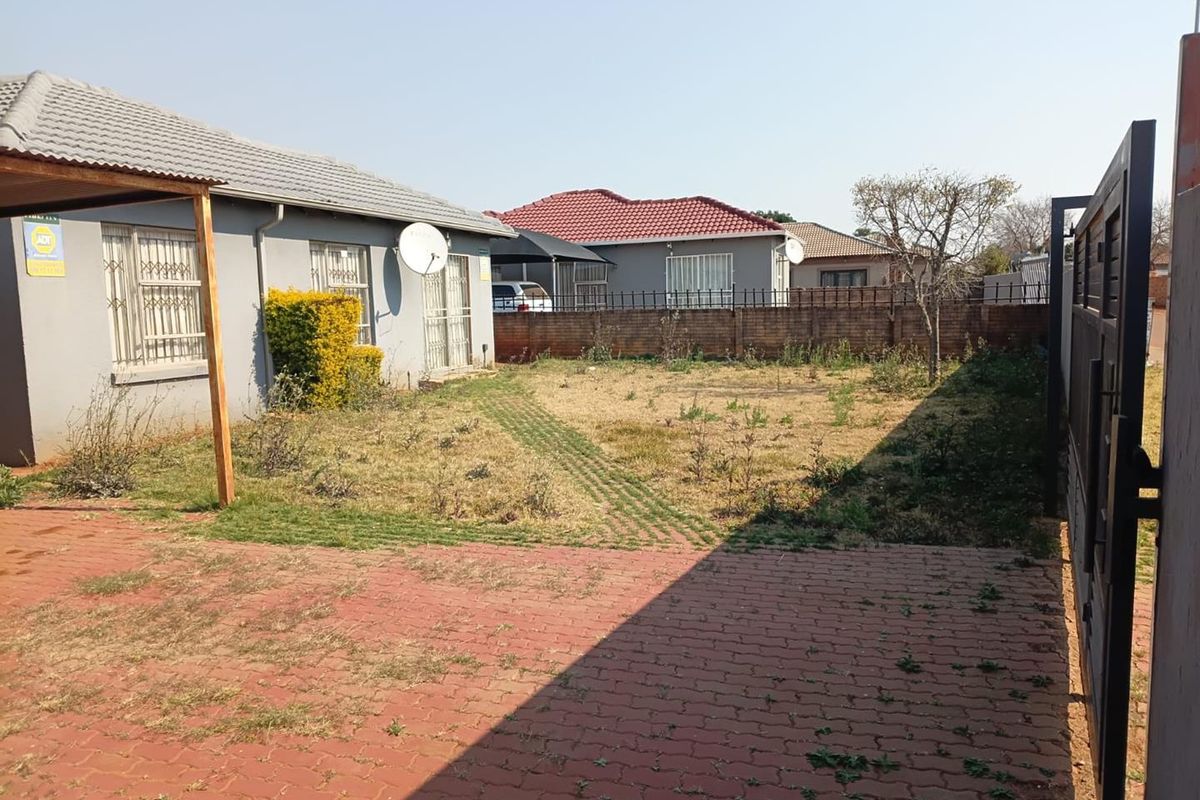 A rear exterior view of the property featuring a paved driveway area, a large garden space, and perimeter walling.