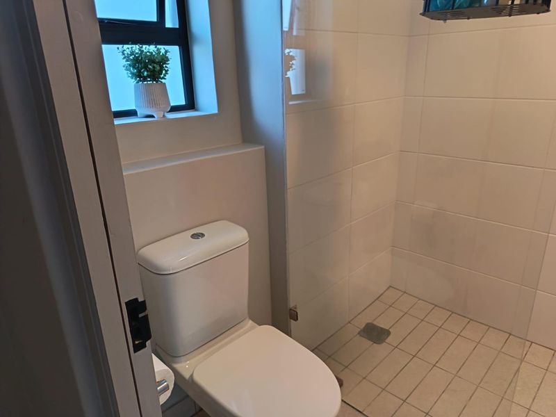 A clean, functional bathroom featuring a modern toilet, a walk-in shower with a glass screen, and neutral wall and floor tiling.