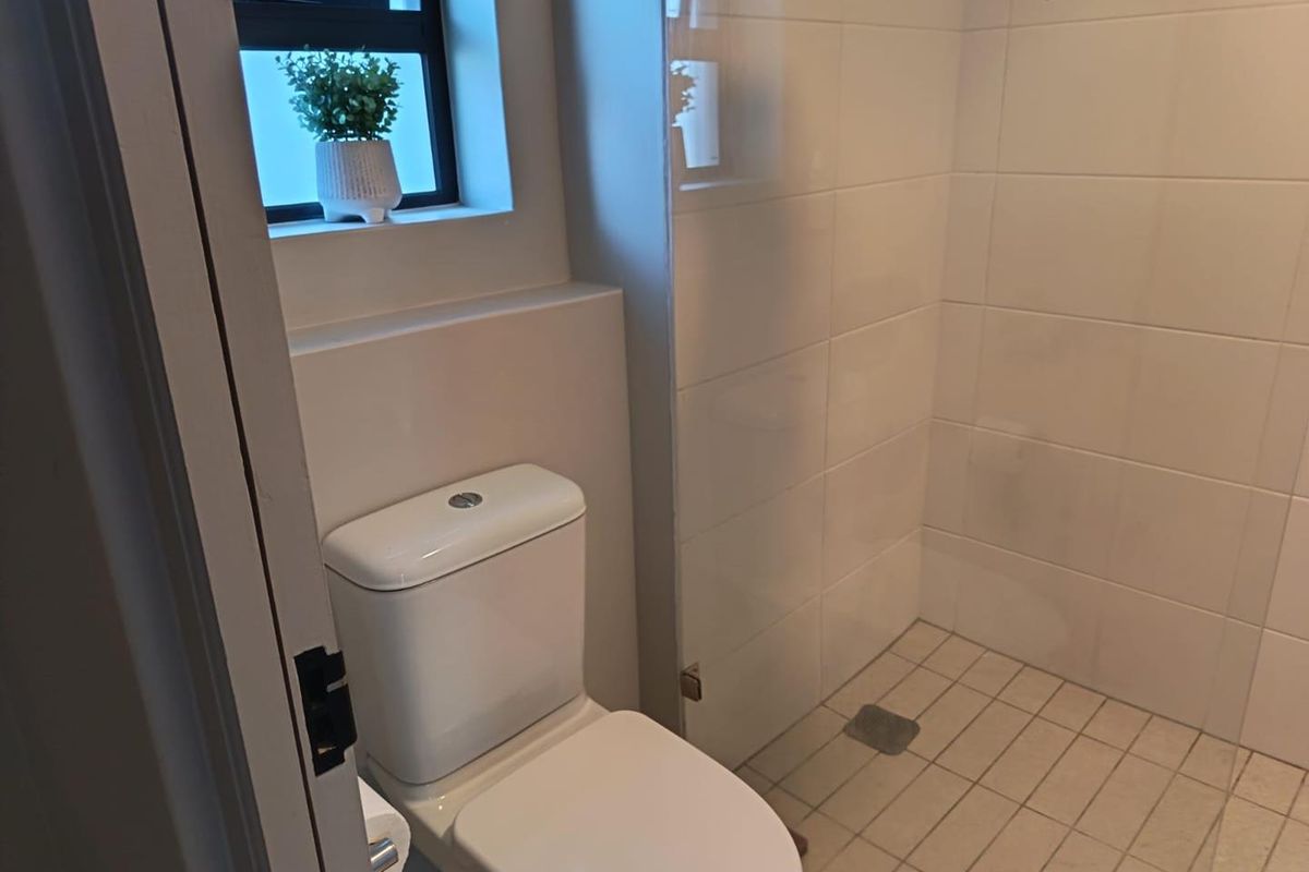 A clean, functional bathroom featuring a modern toilet, a walk-in shower with a glass screen, and neutral wall and floor tiling.