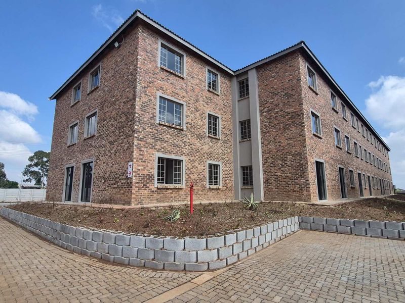 Exterior view of a multi-story apartment building featuring a face brick facade, paved driveway, and landscaped retaining wall area.
