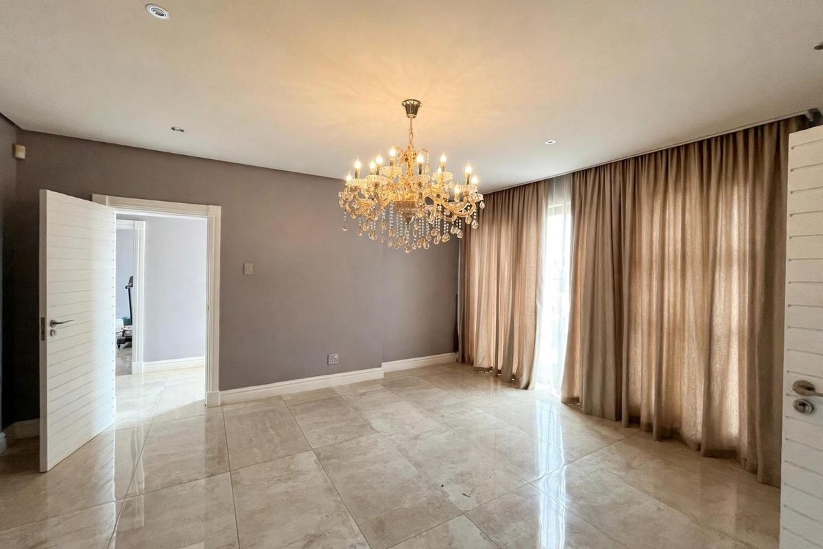 Spacious living area featuring polished porcelain tile flooring, elegant crystal chandelier lighting, and neutral wall finishes with floor-to-ceiling curtain tracks.