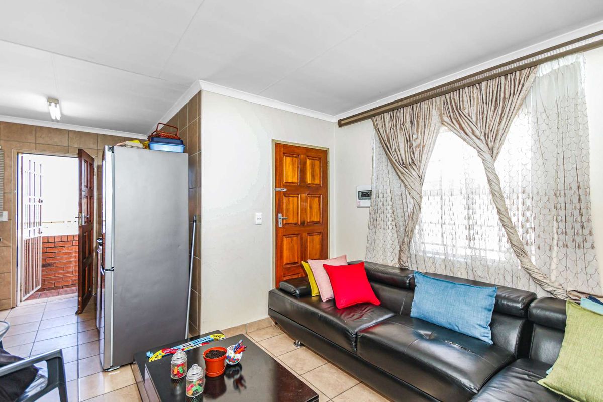 A living room area featuring tiled flooring, a wooden door, and a window with curtaining, providing access to an adjacent tiled outdoor space.
