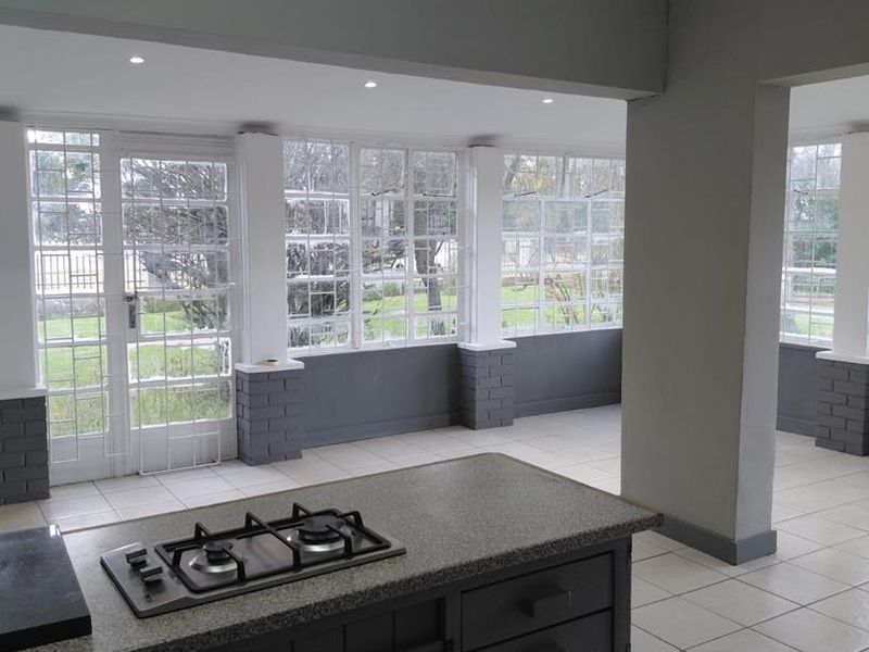 Spacious open-plan living area featuring a central kitchen island with a gas hob, tiled flooring, and abundant natural light through large multi-pane windows.