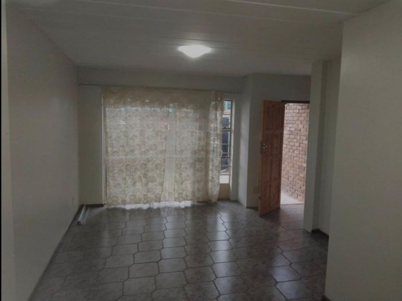 An empty living room featuring tiled flooring and direct access to an exterior area through a timber door.