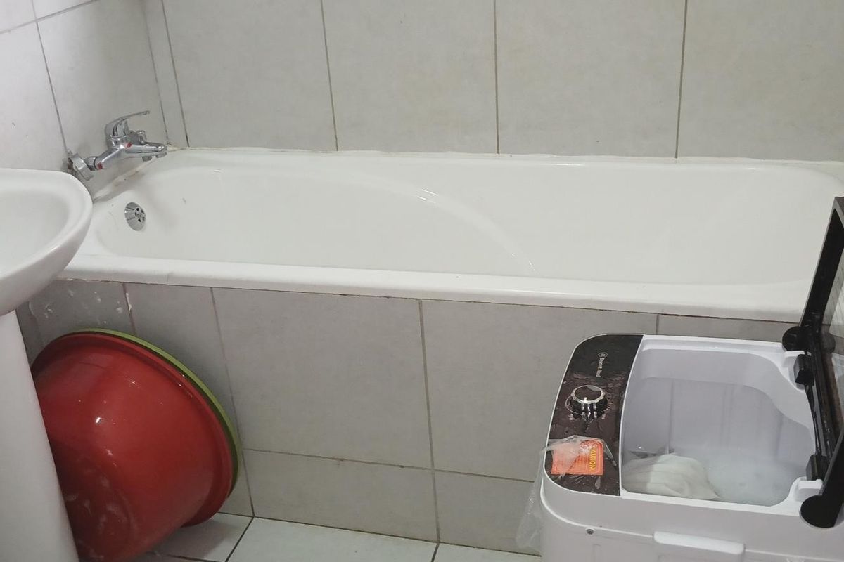 A functional bathroom featuring a pedestal basin, bathtub, and neutral ceramic tiling throughout.