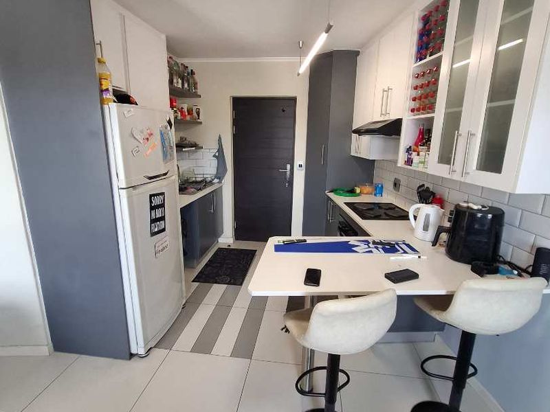 Modern kitchen featuring white cabinetry, subway tile backsplash, built-in hob with extractor, and a functional breakfast bar area with tiled flooring.