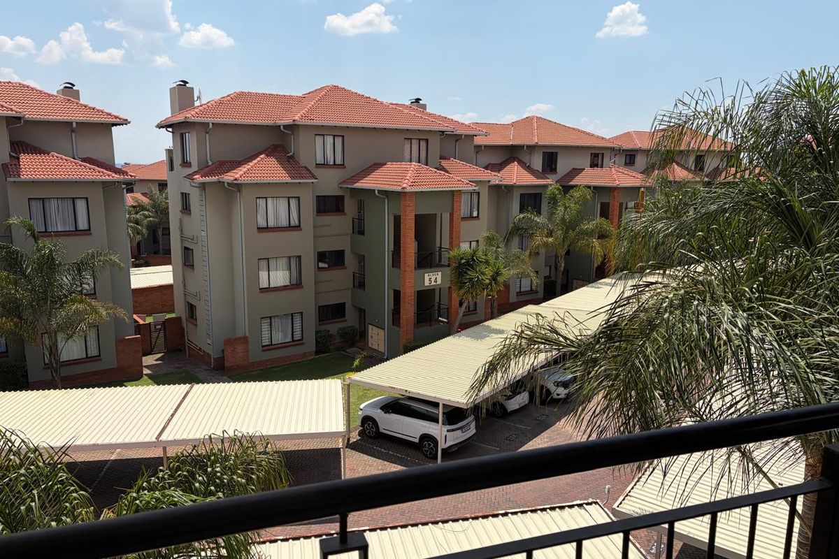 View of the apartment complex exterior featuring multi-story residential blocks, tiled roofing, and covered parking facilities within a landscaped estate setting.