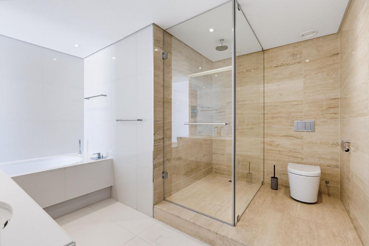 Modern bathroom featuring a built-in bathtub, a spacious glass-enclosed shower, and a wall-mounted toilet with elegant travertine and white tile finishes.