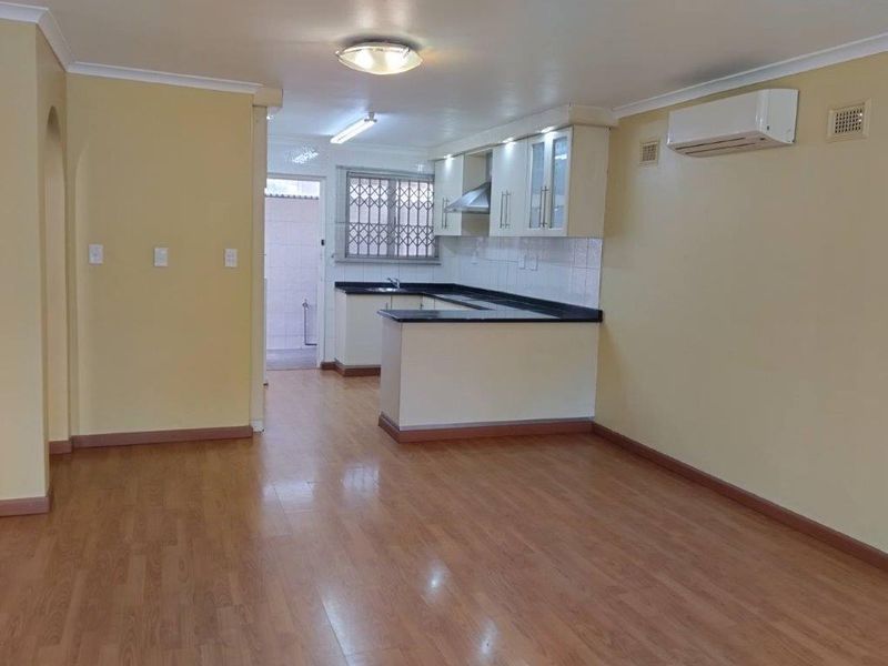An open-plan living and kitchen area featuring laminate flooring, neutral walls, and a functional kitchen with granite countertops and built-in cabinetry.
