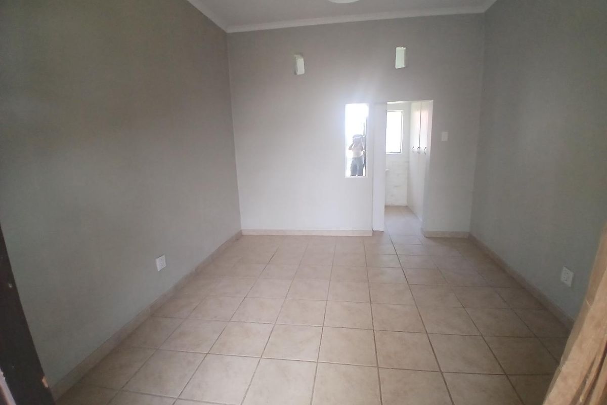 An empty, neutral-toned living area featuring ceramic floor tiles, built-in storage, and direct access to an adjacent room.