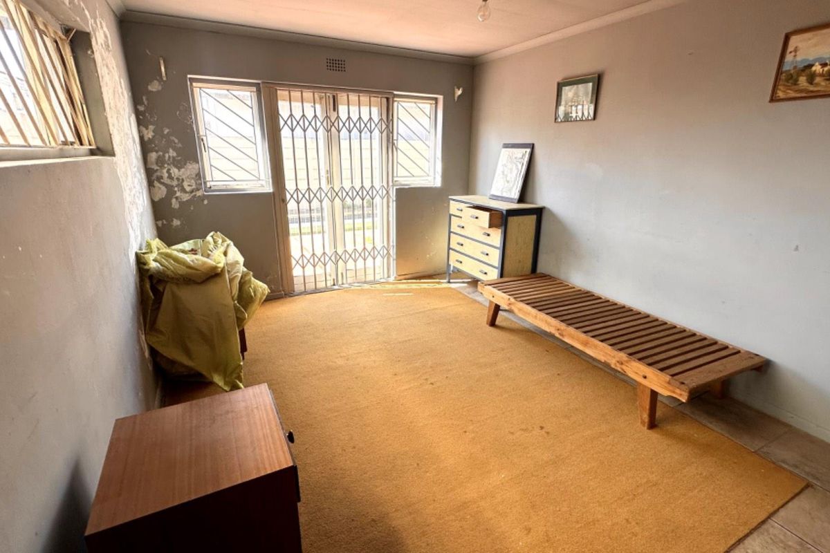 A living area featuring tiled flooring, security gates, and burglar bars, currently requiring wall repairs and cosmetic updates.