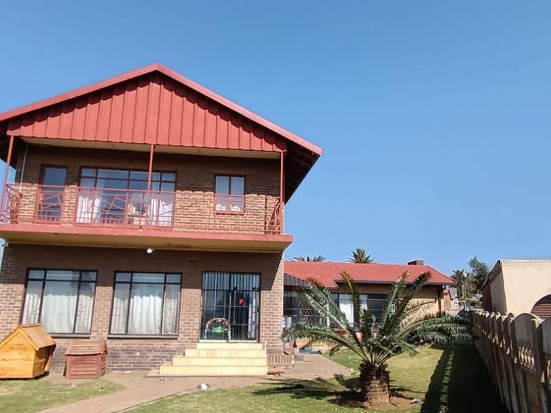 Rear view of a two-story brick house featuring a metal roof, upper-level balcony with metal railings, and a spacious garden area.