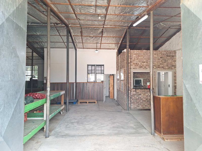 Spacious industrial utility area featuring exposed steel roof structure, concrete flooring, and a brick partition wall, suitable for workshop or storage use.