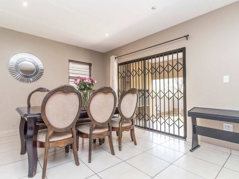 A bright dining area featuring neutral walls, tiled flooring, recessed lighting, and a sliding security gate providing access to the outdoor patio.