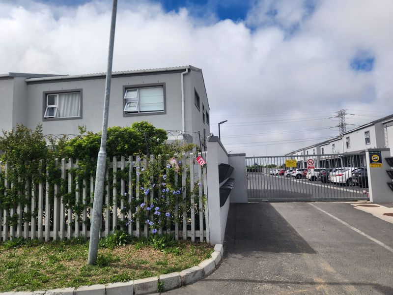 Front entrance view of the apartment complex featuring a secure gated access point, perimeter fencing, and paved driveway.