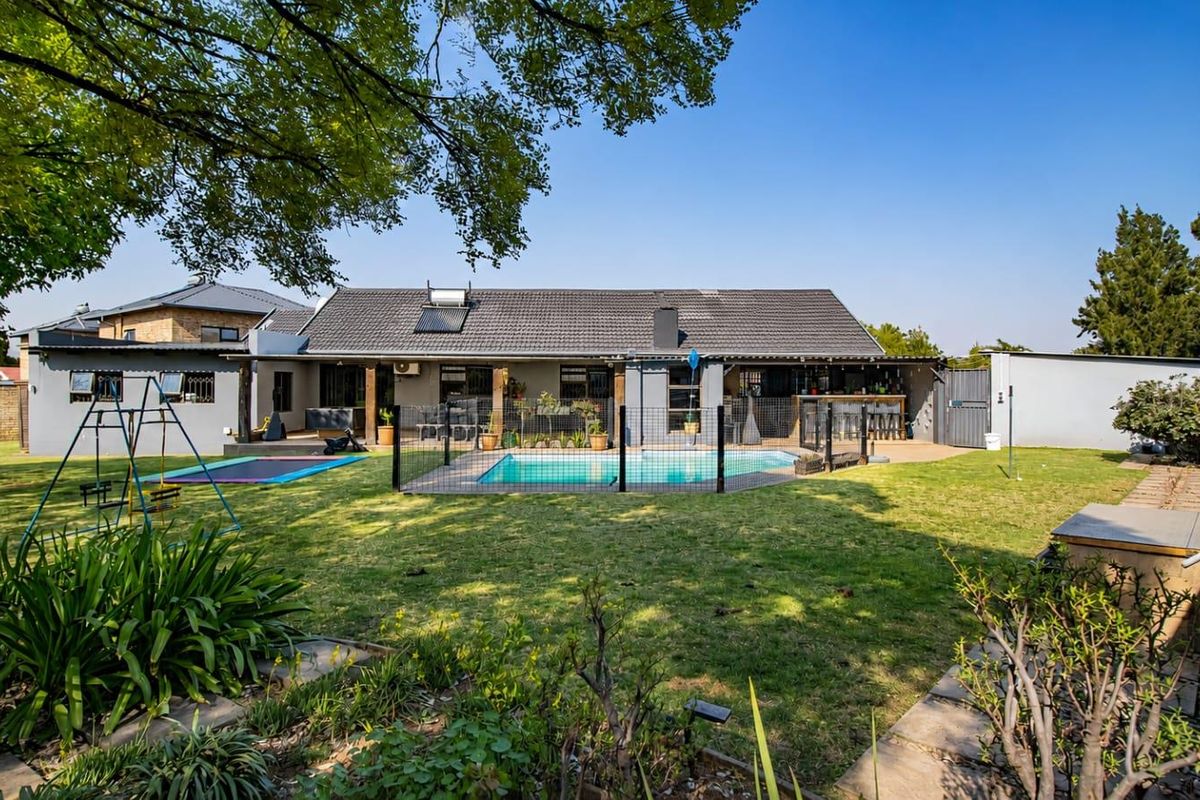 Rear view of the property featuring a landscaped garden, swimming pool with safety fencing, and a covered patio area under a tiled roof.