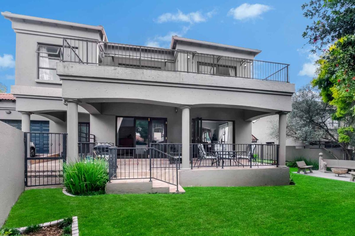 Rear view of a two-story residence featuring a covered ground-floor patio, an upper-level balcony with metal railings, and a well-maintained lawn.