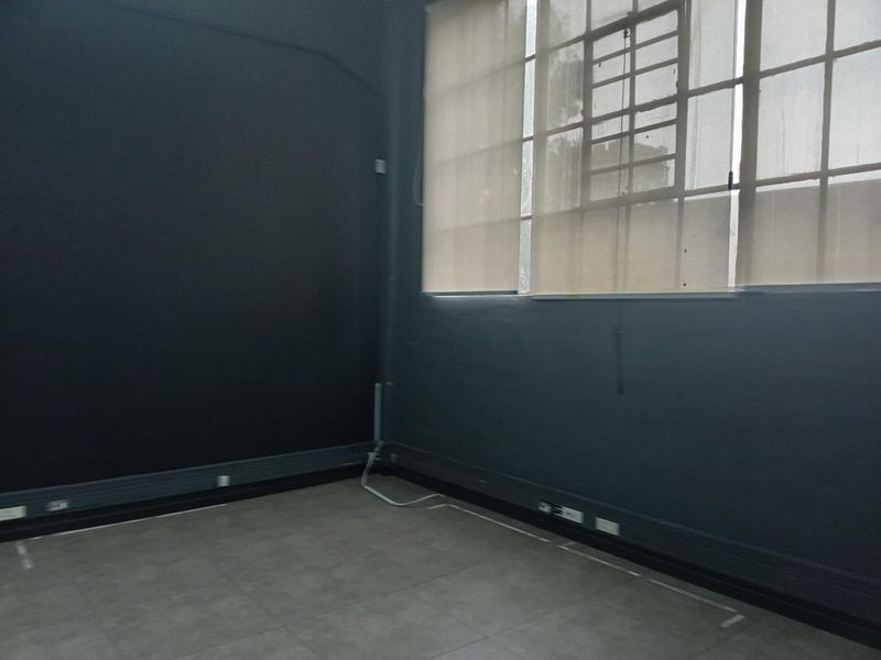 An empty office space featuring dark painted walls, industrial-style windows with roller blinds, and tiled flooring, suitable for a professional workspace.