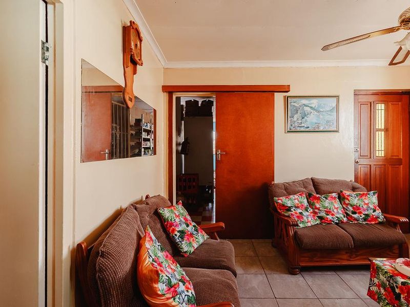 A living room featuring tiled flooring, a ceiling fan, and a sliding door, presenting a dated aesthetic with potential for modernization.