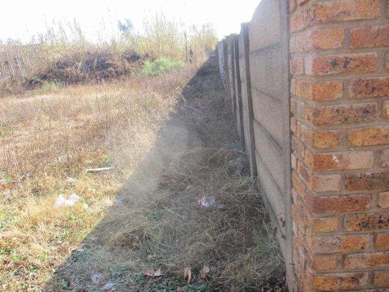 A view of the vacant residential land showing a precast concrete boundary wall and a face brick pillar along the property perimeter.