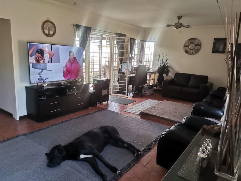 A spacious living room featuring tiled flooring, a ceiling fan, and direct access to the outdoor area through a sliding glass door with security gate.