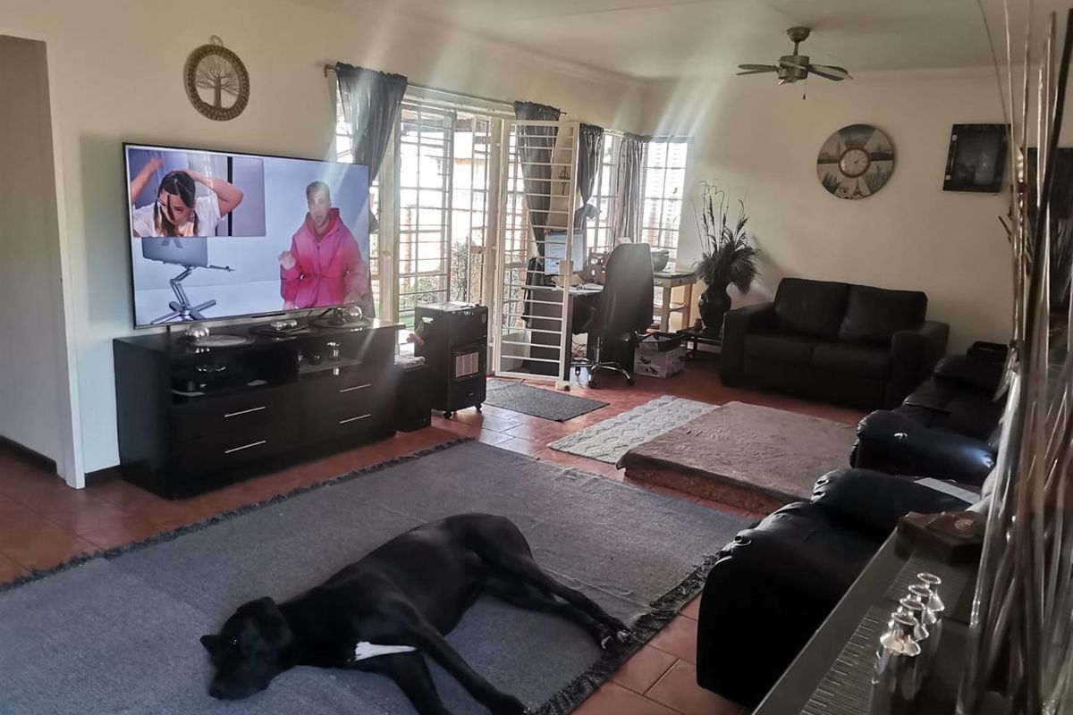 A spacious living room featuring tiled flooring, a ceiling fan, and direct access to the outdoor area through a sliding glass door with security gate.