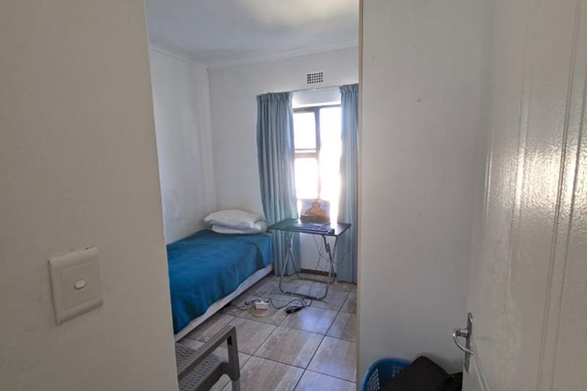 A compact bedroom featuring tiled flooring, a window with natural light, and a standard ceiling light fixture.