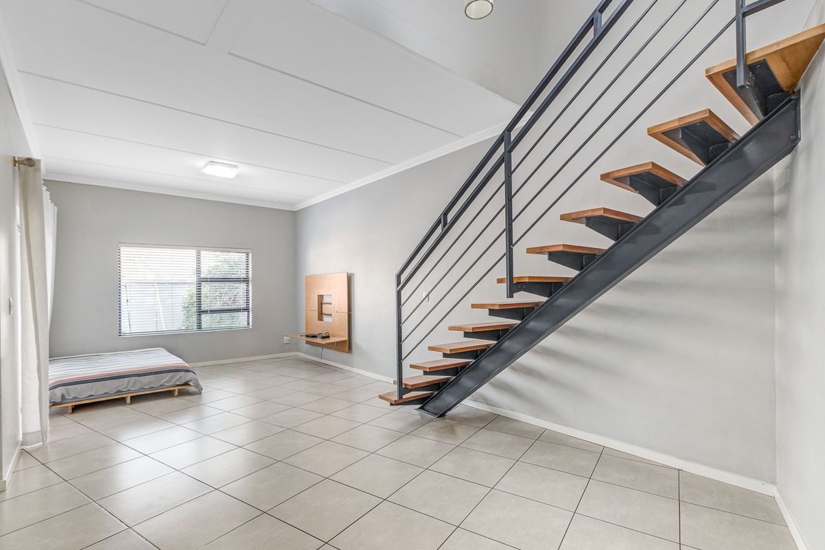 Spacious open-plan living area featuring modern tiled flooring and a striking open-tread staircase with a metal balustrade.