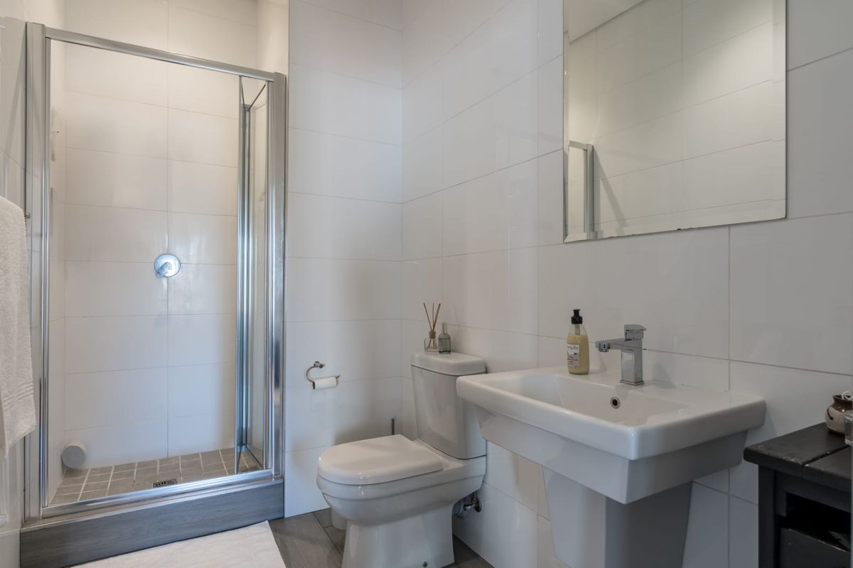 A clean, modern bathroom featuring a glass-enclosed shower, pedestal sink, and white wall tiling.