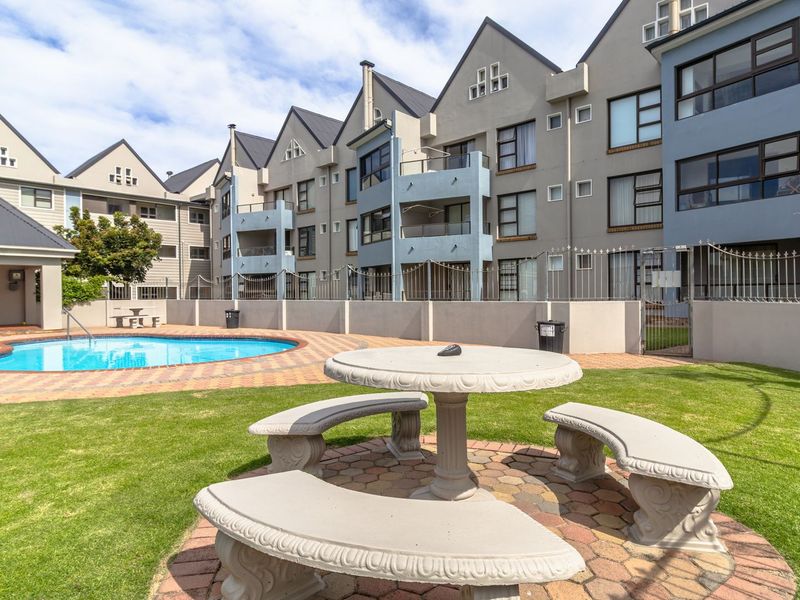 A well-maintained communal pool area featuring a paved surround, landscaped lawn, and views of the multi-story apartment building facade.