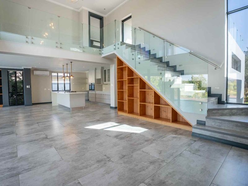 Spacious open-plan living area featuring a modern staircase with glass balustrades, built-in under-stair shelving, and a contemporary kitchen with a central island.