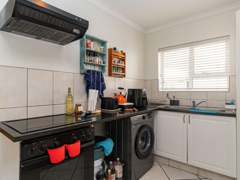 Compact kitchen featuring black granite countertops, white cabinetry, tiled backsplash, integrated stove with extractor fan, and a stainless steel sink.