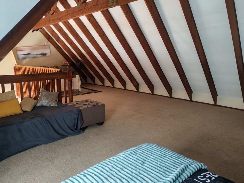 Spacious loft-style bedroom featuring exposed timber rafters, a timber balustrade, and carpeted flooring, offering a unique architectural character.
