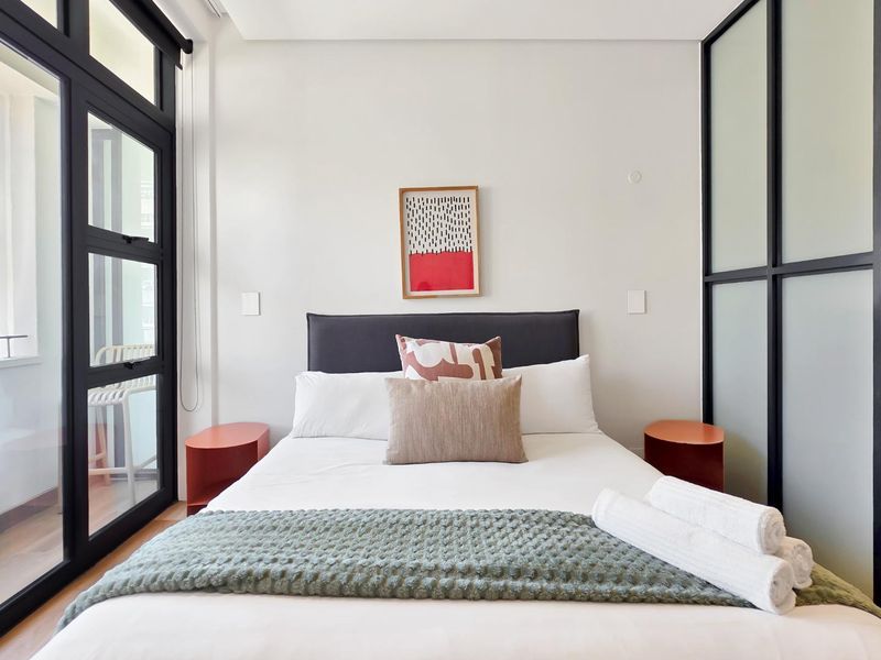 Modern bedroom featuring sleek black-framed glass doors leading to a balcony and a contemporary frosted glass partition wall.