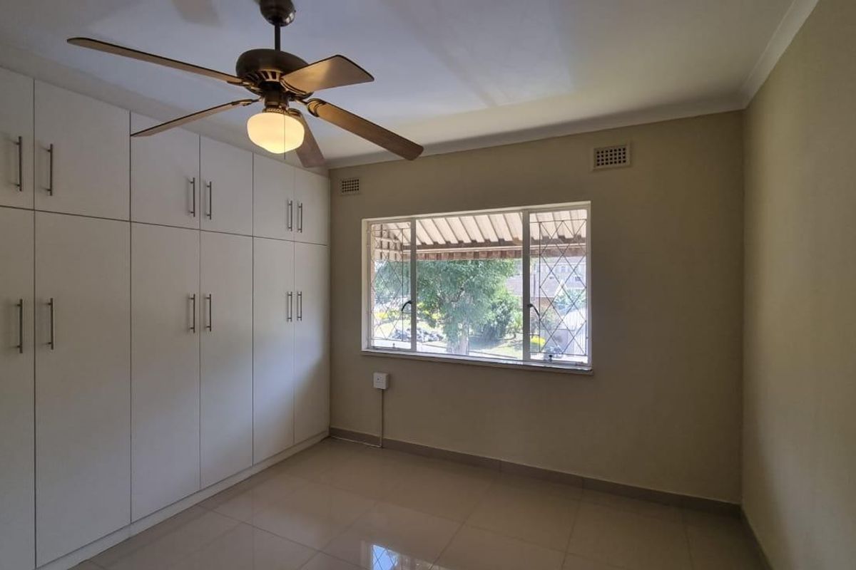 A clean, empty bedroom featuring neutral tiled flooring, ample built-in cupboard storage, and a ceiling fan.