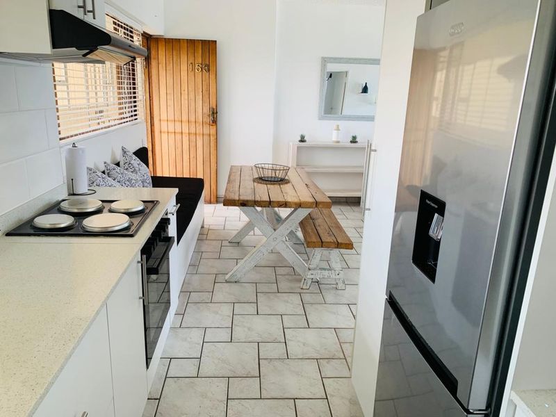 Open-plan kitchen and dining area featuring tiled flooring, built-in cabinetry with integrated appliances, and direct access to the main entrance.