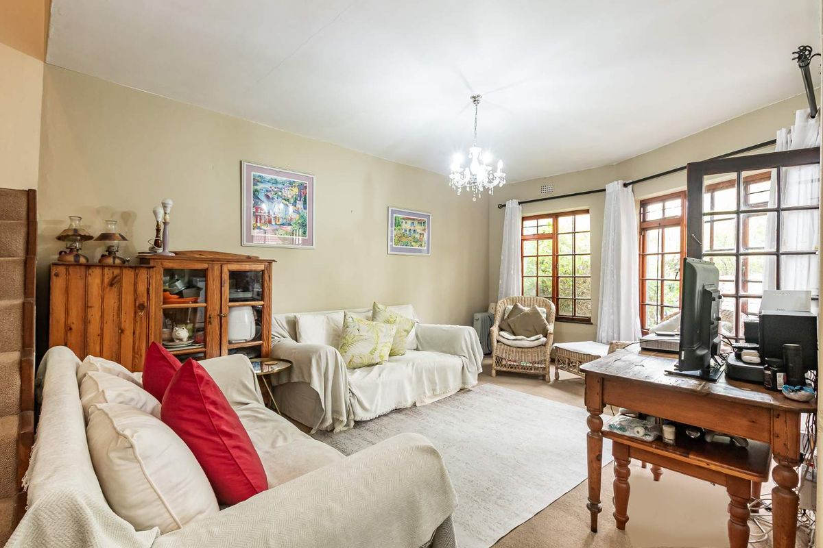 A comfortable living room featuring timber-framed windows, neutral wall tones, and a central chandelier, offering a warm and inviting space.