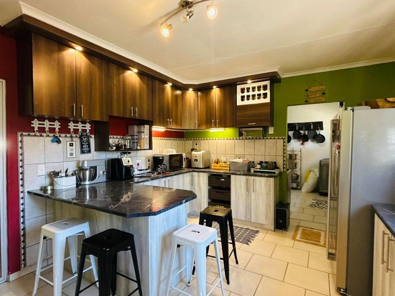 A functional kitchen featuring dark wood-look cabinetry, marble-effect countertops, a breakfast bar, and tiled flooring, with an adjacent scullery area.