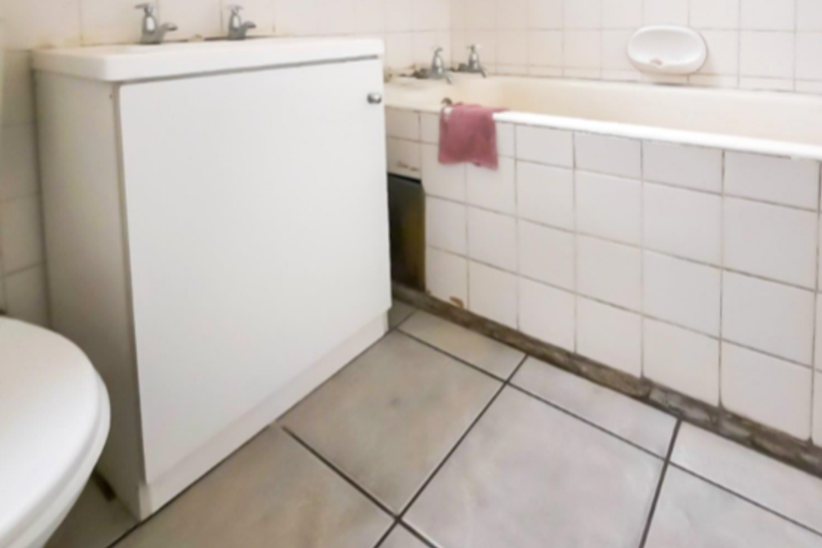 A dated bathroom featuring a built-in bathtub with tiled surround, a vanity cabinet with integrated sink, and ceramic floor tiling.
