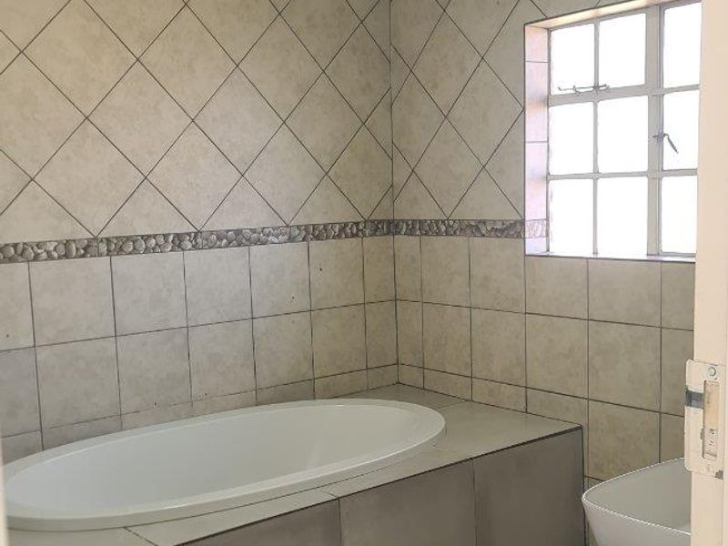 A functional bathroom featuring a built-in bathtub, vessel sink with vanity, and neutral tiled finishes throughout.