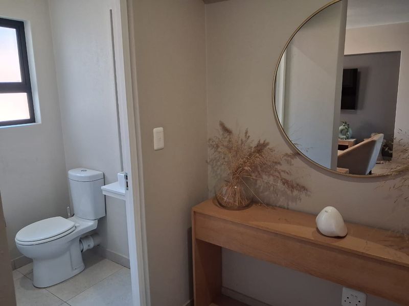 A clean and well-maintained bathroom featuring a modern toilet, tiled flooring, and a window, adjacent to a hallway area with a console table.